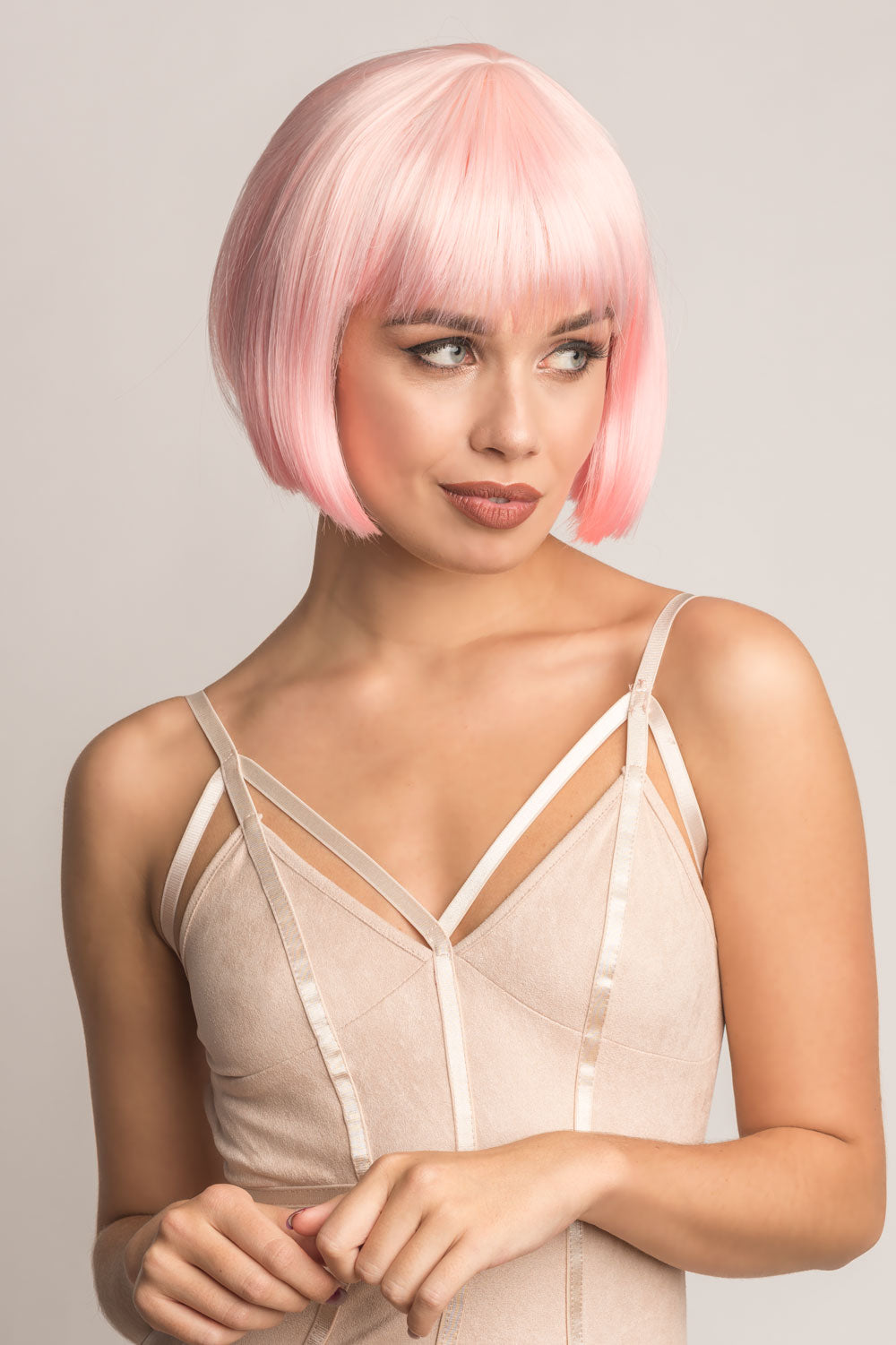 A person wearing a short pink bob wig with a pale pink and platinum ombre effect. The wig features a blunt cut that falls to the chin with inward curling layers, and the person is dressed in a beige top. Short pink bob wig (ombre: pale pink and platinum): Louisa